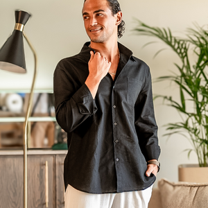 Man wearing a black button-up shirt standing indoors next to a lamp and plant