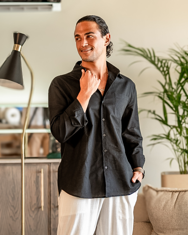 Man wearing a black button-up shirt standing indoors next to a lamp and plant