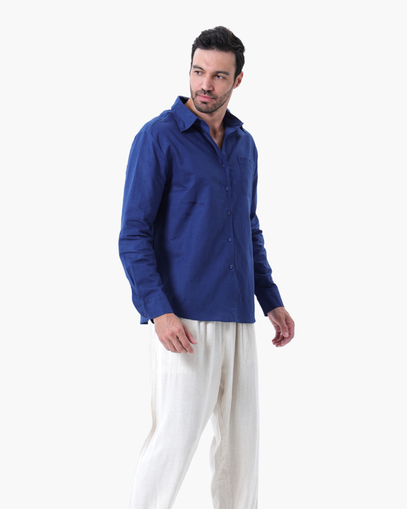 Man wearing a blue long-sleeve button-up shirt and white loose pants standing against white background