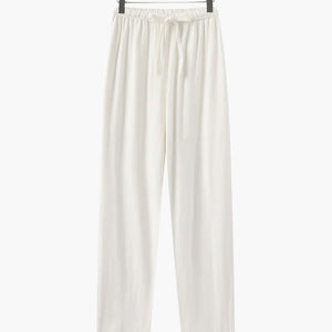 White casual loose fit pants with elastic waistband and drawstring hanging on wooden hanger