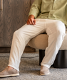 Man wearing beige casual pants and light brown slip-on shoes sitting on a beige cushioned stool